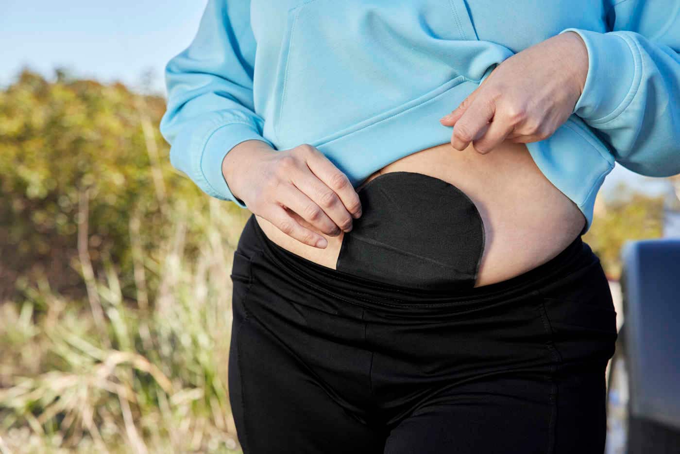 Ausschnitt einer Frau mit schwarzem Stomabeutel am Bauch und hellblauem Pullover