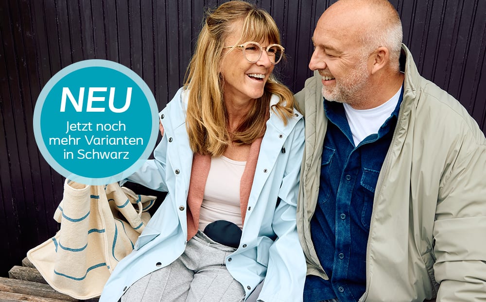 Stomaträgerin mit schwarzen Stomabeutel am Bauch sitzt lachend neben ihrem Mann